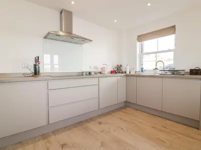 a kitchen with white cabinets and a wooden floor at Gwel Nans in St. Agnes