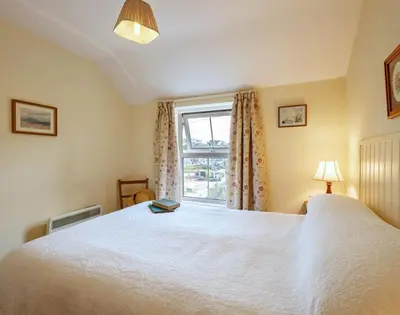 a bedroom with a large white bed and a window at Coppingers Cottage in Polzeath