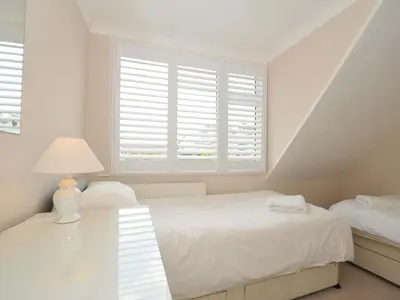 a white bedroom with two beds and a window at Sunset in Polzeath