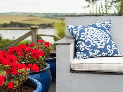 a blue and white pillow sitting on a bench with red flowers at Little Strand in Padstow