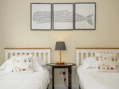 two beds with white sheets and a table with a lamp at Trevega in Polzeath