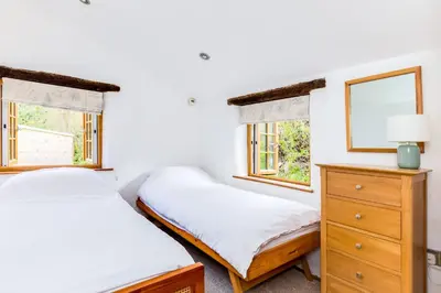 two beds in a room with two windows at Dingles Cottage in Saint Minver