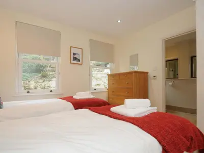 a bedroom with three beds and a dresser and two windows at Pendaveli in Polzeath