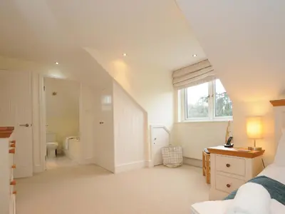 a white bedroom with a bed and a bathroom at Pendaveli in Polzeath