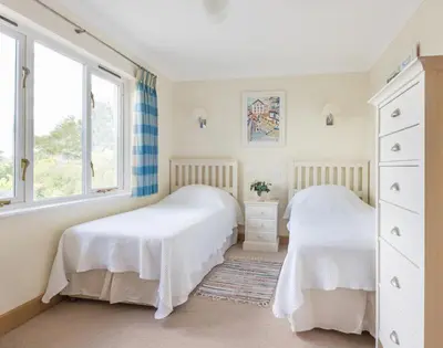 two beds in a bedroom with two windows at Ragleighs in Polzeath