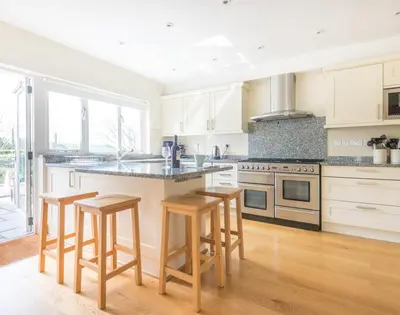 a kitchen with white cabinets and a island with bar stools at Ragleighs in Polzeath