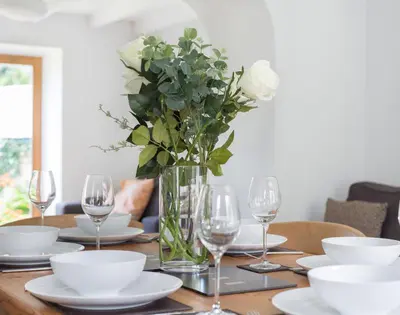 a table with plates and glasses and a vase with flowers at Conifers in Saint Minver