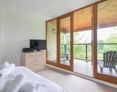 a bedroom with a bed and a balcony with a television at Conifers in Saint Minver