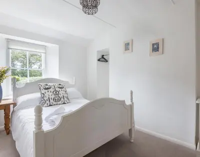 a white bedroom with a white bed and a window at Conifers in Saint Minver