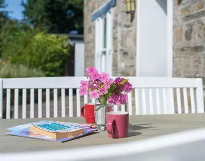 a table with a vase of flowers and a book at Conifers in Saint Minver