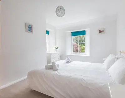 a white bedroom with a large white bed with a window at Conifers in Saint Minver