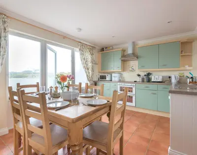 a kitchen with a wooden table with chairs and a kitchen with green cabinets at Kirra in Polzeath