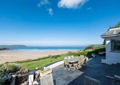 a patio with a table and chairs and a beach at Treverden in Polzeath