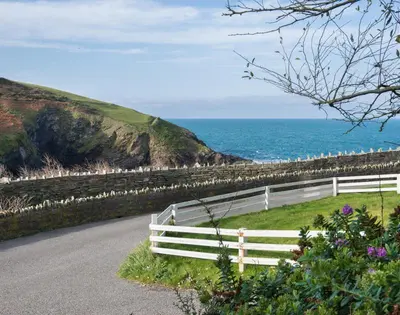a white fence on a road next to the ocean at Beehive Cottage in Port Isaac