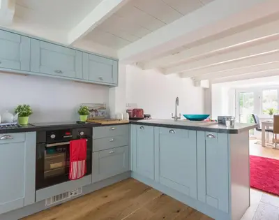 a kitchen with blue cabinets and a red rug at Beehive Cottage in Port Isaac
