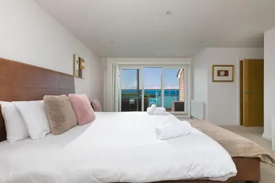 a bedroom with a large white bed with a large window at Sandbanks in Penzance
