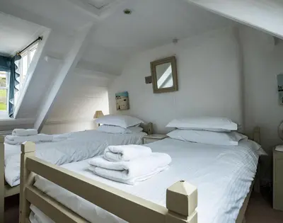 two beds in a white room with towels on them at April Cottage in Port Isaac