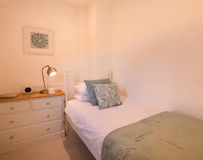 a bedroom with a bed and a dresser with a lamp at Kipper Cottage in Port Isaac