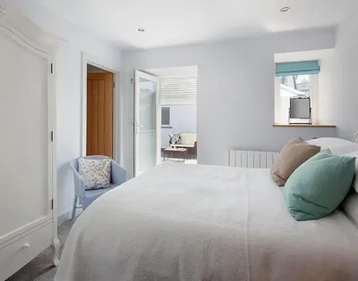 a white bedroom with a large bed and a chair at The Crows Nest in Port Isaac