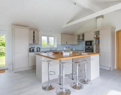 a white kitchen with a island with bar stools at Penny Liggan in Padstow