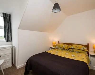 a bedroom with a bed with a black blanket and yellow pillows at Pinewood 14 in Polzeath