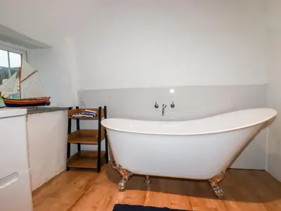 a white bath tub in a room with a table at Downrow Barn in Tintagel