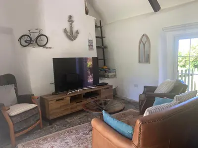 a living room with a flat screen tv and chairs at Downrow Barn in Tintagel