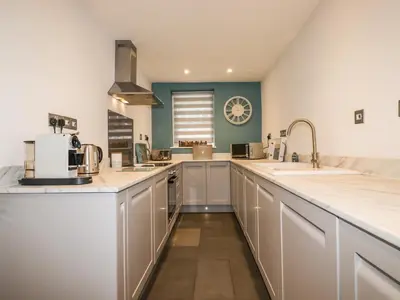 a large kitchen with white cabinets and a clock on the wall at Ludgvan Cottage in Gorran Haven