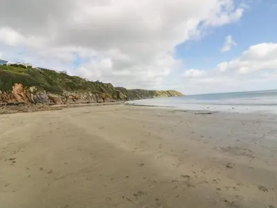 a beach with sand and the ocean on a cloudy day at Ludgvan Cottage in Gorran Haven