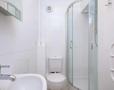a white bathroom with a toilet and a glass shower at St Martins Apartment in Saint Minver