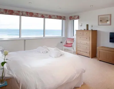 a bedroom with a white bed with a view of the ocean at The White House in Polzeath
