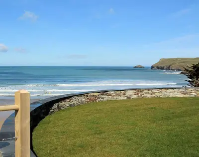 a stone wall next to a beach with the ocean at The White House in Polzeath