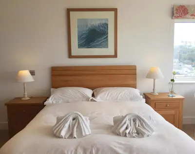 a bedroom with a bed with white sheets and two lamps at The White House in Polzeath