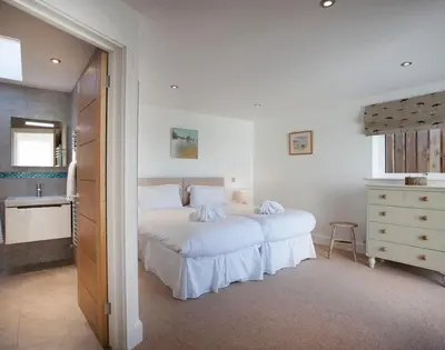 a white bedroom with a large bed and a dresser at The White House in Polzeath
