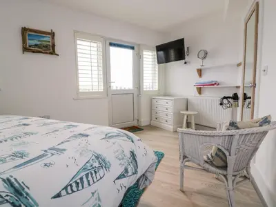 a bedroom with a bed and a chair and windows at Fistral Drift in Newquay