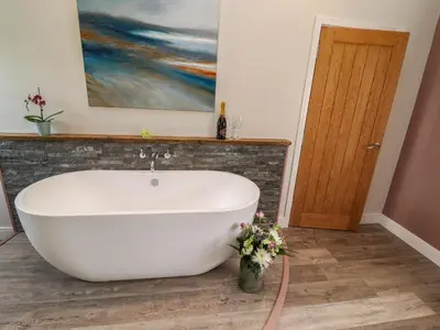 a white bath tub in a bathroom with a painting at The Roost in Helston