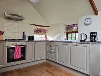 a kitchen with white cabinets and a clock on the wall at Cosy barn on rural smallholding with alpacas, goats & pigs in Stithians