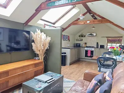 a living room with a tv and a kitchen at Cosy barn on rural smallholding with alpacas, goats & pigs in Stithians