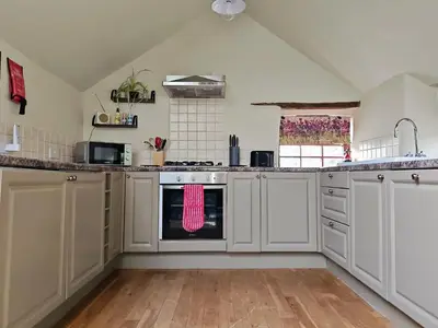 a kitchen with white cabinets and an oven at Cosy barn on rural smallholding with alpacas, goats & pigs in Stithians