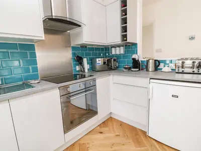 a kitchen with white cabinets and blue tiles at Harbour Hideaway in Looe