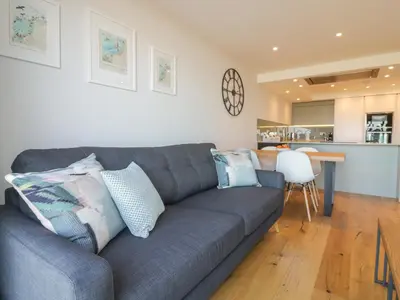 a living room with a gray couch and a kitchen at Fistral Watch in Newquay