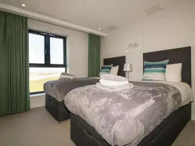 a bedroom with two beds with green curtains and a window at Fistral Watch in Newquay