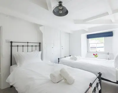 a white bedroom with two beds with white pillows at Bre Cottage in Port Isaac