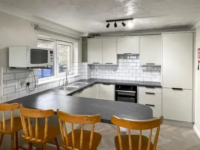 a kitchen with white cabinets and a table and chairs at Apartment 1 Waterrs Edge in Crantock