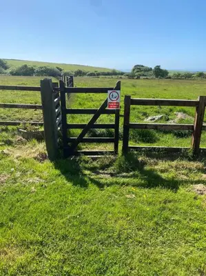 a fence in a field with a sign on it at Venn Down Lakes in Boscastle