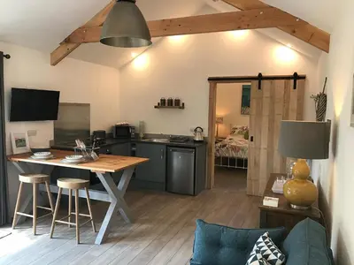 a living room with a table and a kitchen at The Potting Shed in St Austell