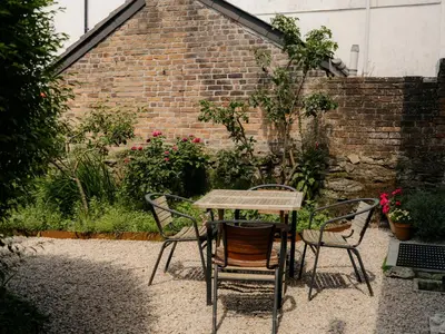 a table and chairs in a garden with a brick wall at Enchanted Rose Garden House in Falmouth