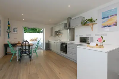 a kitchen with white cabinets and a table with chairs at Hillywych Studio in Redruth