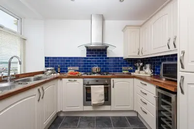 a kitchen with white cabinets and blue tiles at Cormorant Views, Marazion in Marazion