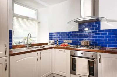 a kitchen with white cabinets and blue tiles at Cormorant Views, Marazion in Marazion